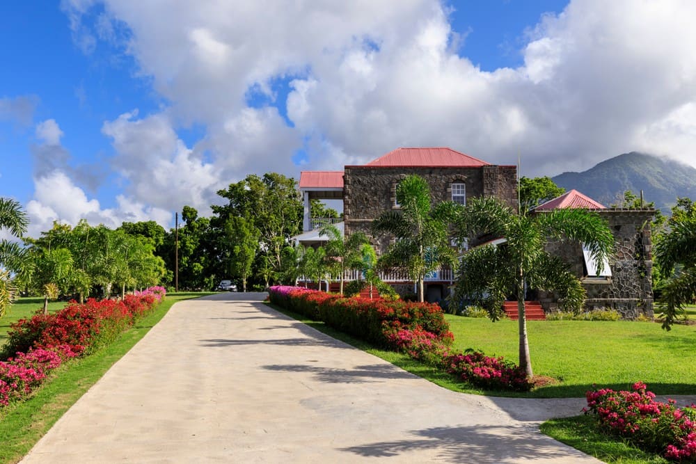 A volcanic-stone plantation house with a red roof beneath Nevis Peak